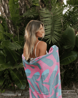 Woman wrapped in a pink and blue patterned towel with tropical plants in the background