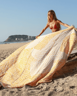 Woman on a beach with a large yellow and white patterned towel