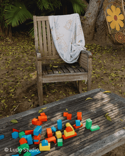 Colorful building blocks on a wooden table with a wooden chair and blanket in the background.