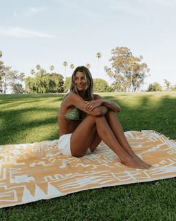 Woman in a bikini sitting on a patterned blanket in a park