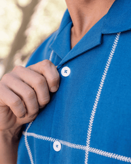 Close-up of a person wearing a blue shirt with white embroidery, focusing on a button.