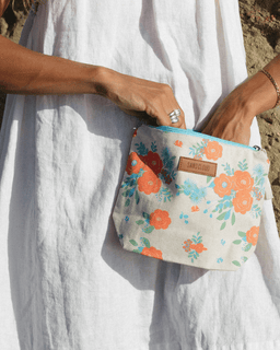 Floral pouch held by a person wearing a white dress on a beach.