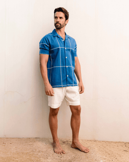Man wearing a blue checkered shirt and white shorts against a plain background