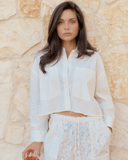 Woman wearing a light-colored outfit against a stone wall.