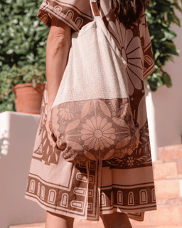Person wearing a patterned dress holding a white bag with floral design outdoors.