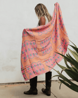 Person holding a large pink floral-patterned towel against a white wall.