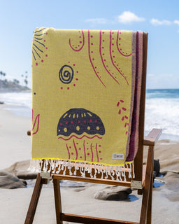 Yellow beach towel with jellyfish design on a wooden chair at the beach.