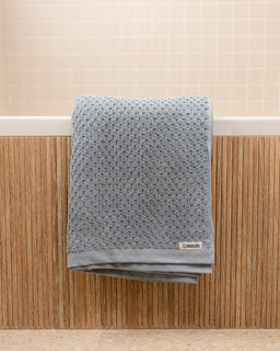 Gray textured towel hanging on a wooden rack with a beige wall in the background