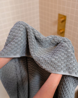 Person holding a textured gray towel in a bathroom setting