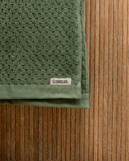 Green textured towel with a brand label on a wooden surface