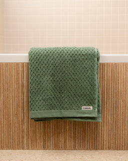 Green textured towel on a wooden surface with a neutral background