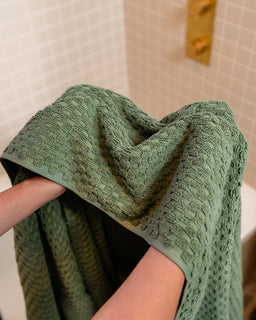 Green textured towel held by a person in a bathroom setting