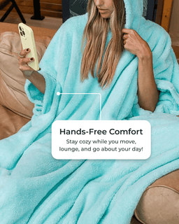 A woman wrapped in a plush light aqua blue hooded blanket sits on a couch, holding a phone. A text overlay reads, 'Hands-Free Comfort.