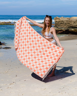 Woman holding a pink and white checkered towel on a beach