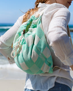 Person wearing a light blue drawstring bag with geometric pattern on a beach.