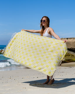Woman holding a yellow and white patterned towel on a beach