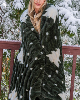 Girl on with snowy trees behind her and wrapped up in green christmas tree print drift blanket