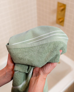 Person holding a green towel with white stripes in front of a bathroom sink.