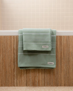 Green towel with a brand label hanging on a wooden surface.