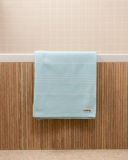 Light blue towel hanging on a wooden rack with a beige wall in the background