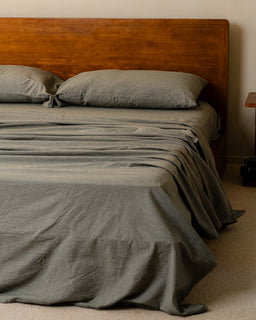 Bed with moss bedding and wooden headboard against a beige wall