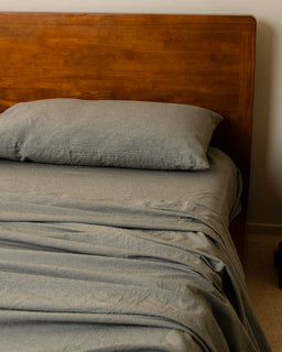 Bed with moss bedding and a wooden headboard against a beige wall.