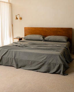 Bedroom with a wooden bed and moss bedding, featuring a wall lamp.