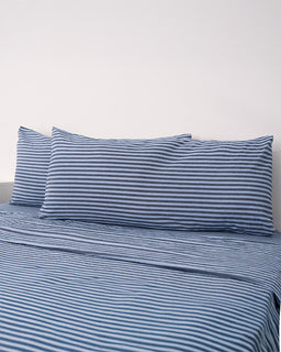 Blue and white striped bedding set on a bed with a plain background