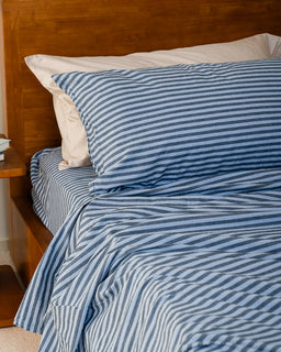 Blue and white striped bedding on a bed with wooden headboard