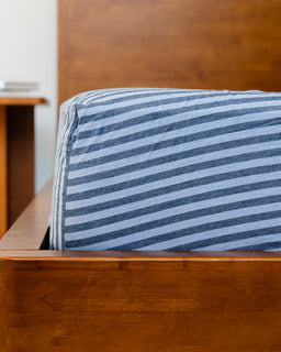 Blue and white striped fitted sheet on a wooden bed frame