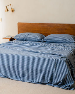 Bed with blue striped bedding and wooden headboard in a room.