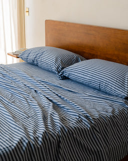 Bed with blue and white striped bedding and pillows in a room.