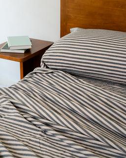 Striped bedding on a bed with a wooden headboard and nightstand.
