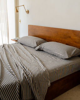 Bed with striped bedding and wooden headboard in a room with a lamp and window.