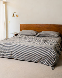 Bed with striped bedding and wooden headboard in a room with a wall sconce.