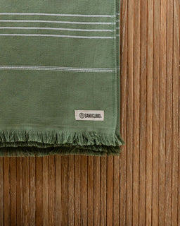 Green towel with white stripes on a wooden surface, featuring a SandCloud label.
