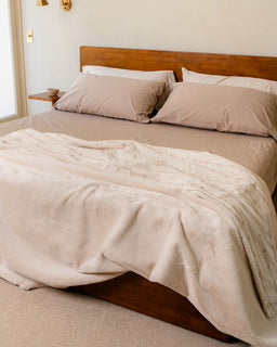 Neatly made bed with beige bedding and pillows in a bedroom setting.