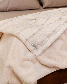 Beige quilted blanket on a bed with a visible brand label.