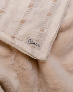 Beige textured blanket with a brand label on a soft beige background
