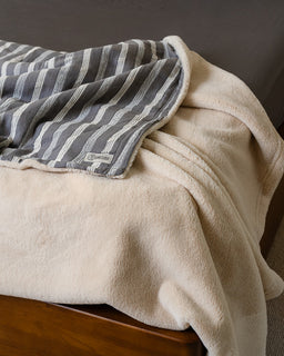 Beige blanket draped over a wooden surface with a striped gray and white blanket on top.