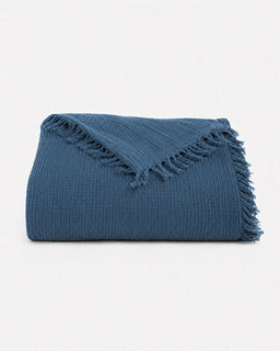 A folded textured blue throw blanket with fringed edges, displayed on a clean white background.