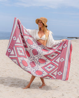 Woman on a beach holding a pink and white patterned towel