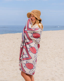 Woman on a beach wrapped in a patterned towel with a straw hat