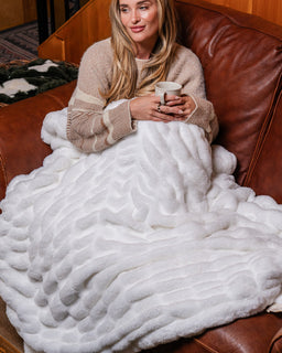 Girl on sofa in cabin with cozy snow colored drift blanket holding a mug