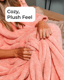 A close-up of a person wrapped in a soft, plush peach-pink blanket, with hands visible and a white text label that reads 'Cozy, Plush Feel'.