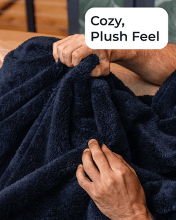 A close-up of a person holding a dark navy plush blanket, with a white text label that reads 'Cozy, Plush Feel' over the top right.