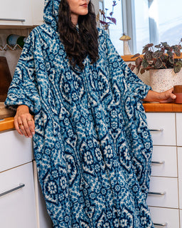 A woman wearing a plush hooded robe with a blue and white bohemian-style geometric pattern, standing in a kitchen environment.