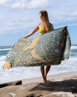 Woman holding a large towel with celestial design on a beach