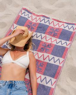 Person lying on a colorful beach towel with geometric pattern on sand