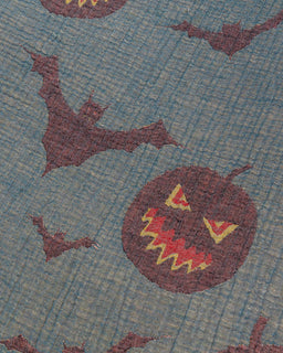 A close-up of a woven textile pattern featuring dark brown bats and jack-o'-lanterns on a muted blue-gray background.
